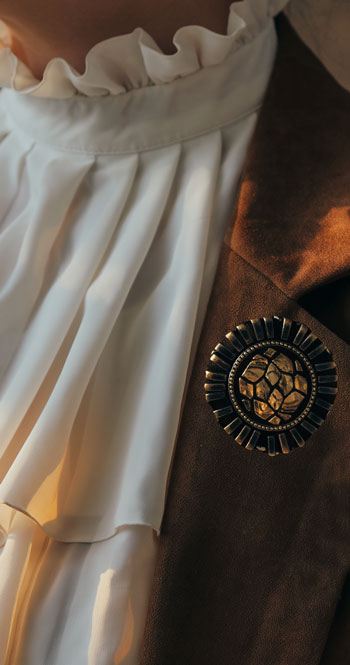 chunky brooch on a brown suede jacket with ruffled shirt